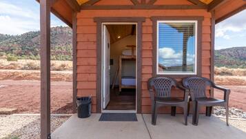 A rustic cabin with a wooden exterior, a door leading to a bedroom, and two plastic chairs outside.