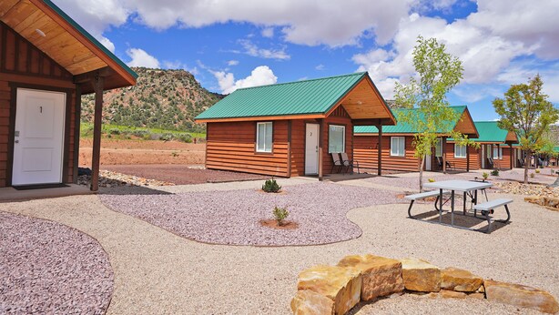 A row of wooden cabins with green roofs, a gravel patio, and a picnic table. - Gooseberry Lodges (Hurricane)
