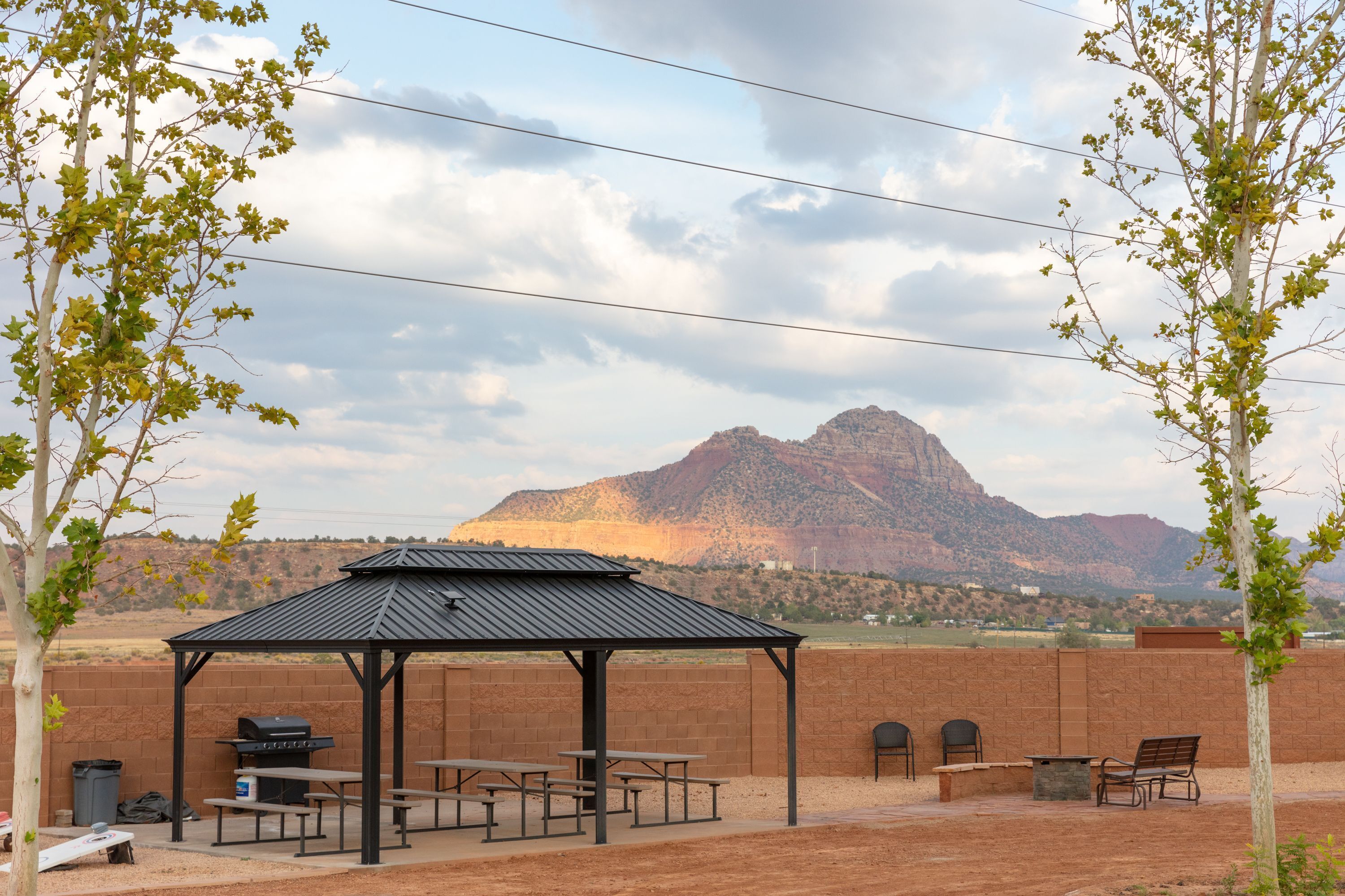 A covered picnic area with tables and benches, a barbecue grill, and a view of a mountain.