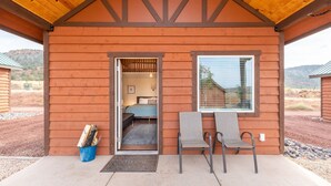 A wooden cabin with a porch, a bed, and two chairs.