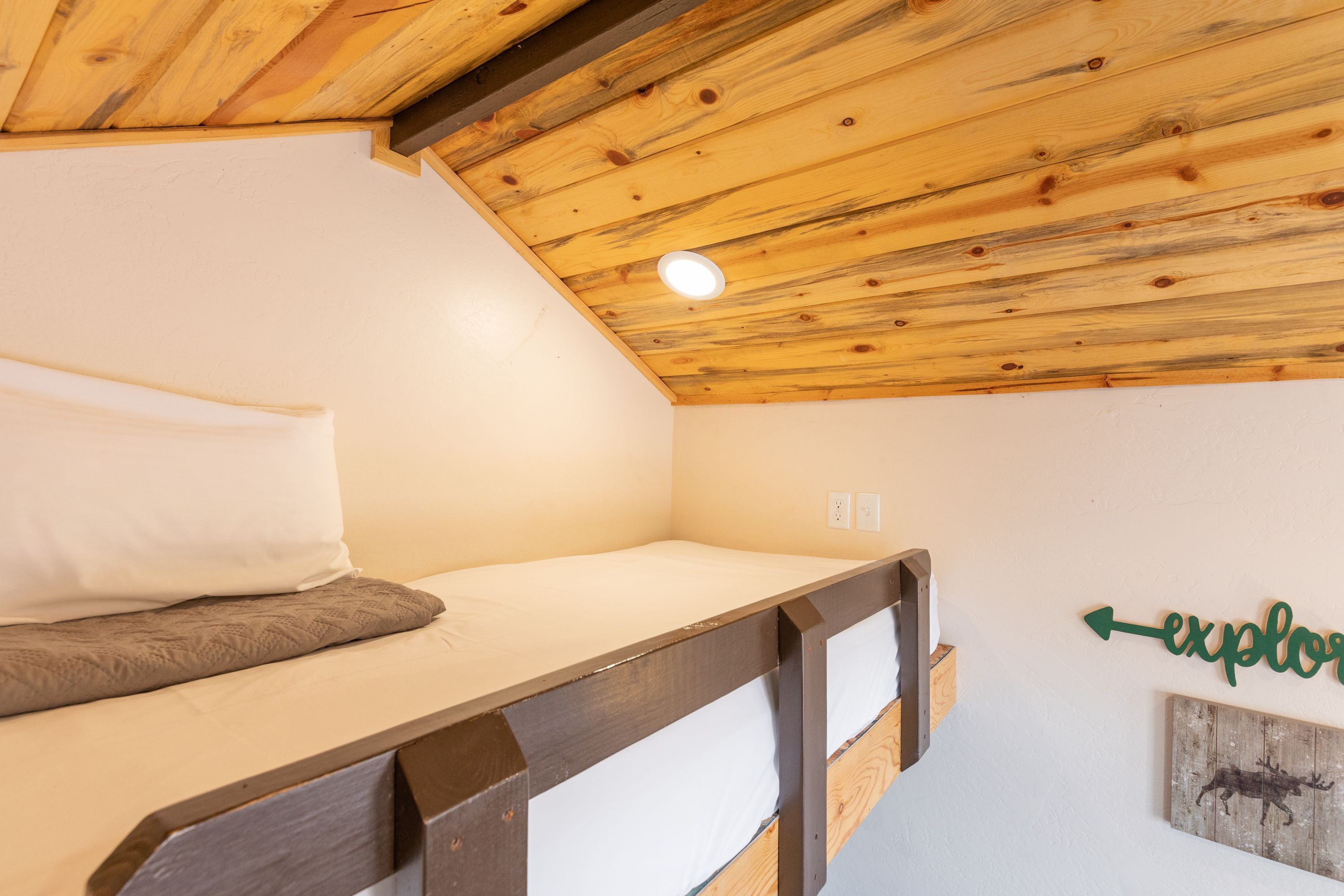 A small, single-bed room with a sloped ceiling and a wooden headboard.