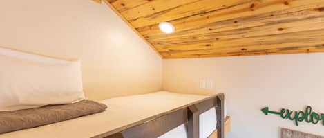 A small, single-bed room with a sloped ceiling and a wooden headboard.