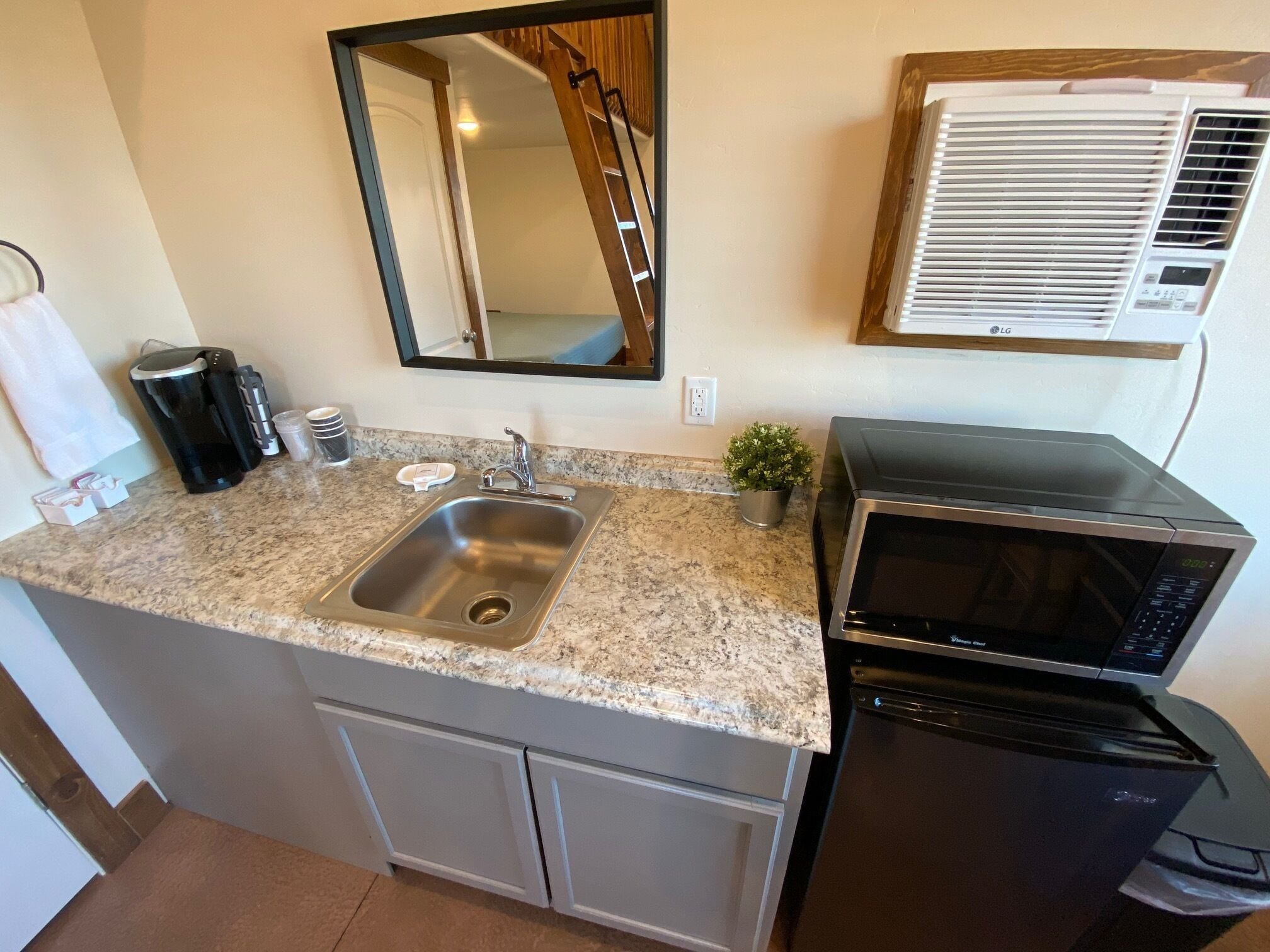 Cocina compacta con encimera de granito, pileta de acero inoxidable y microondas integrado.