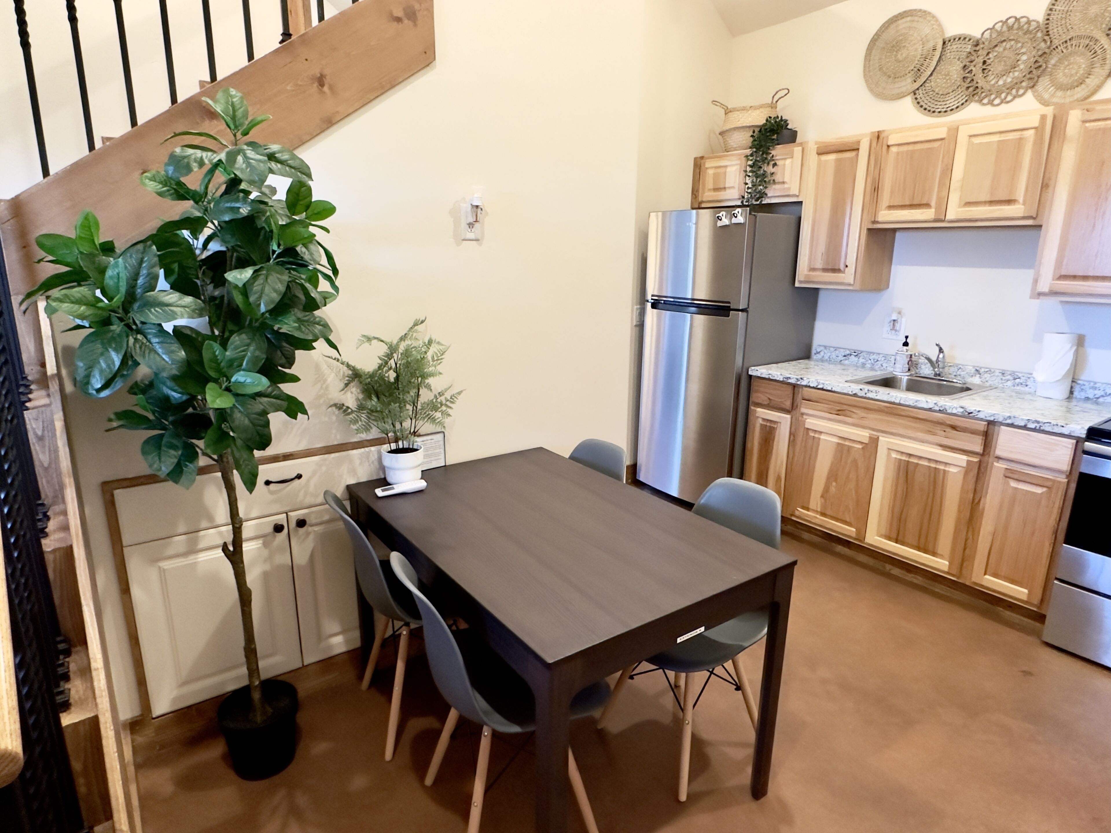 Una cocina moderna con armarios de madera, un refrigerador de acero inoxidable, encimera de granito y una mesa de comedor con sillas.