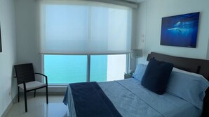 A bedroom with a large bed, a chair, a window with a view of the sea, and a painting on the wall. - Vista 180 grados (Cartagena)