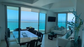 A modern living room with a glass dining table, white sofa, and a large window overlooking the sea. - Vista 180 grados (Cartagena)