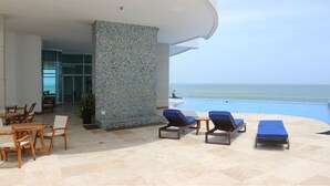 A poolside area with lounge chairs, a table, and a view of the ocean. - Vista 180 grados (Cartagena)