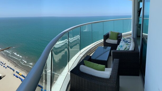 A balcony with wicker furniture and a glass railing overlooking a beach and ocean. - Vista 180 grados (Cartagena)