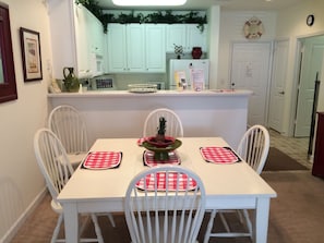 A dining area with a white table and chairs, a pineapple centerpiece, and a kitchen in the background. - 28007 Woodlands Way (Calabash)