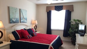 A neatly arranged bedroom with a bed, bedside tables, a television, and a window with curtains. - 28007 Woodlands Way (Calabash)