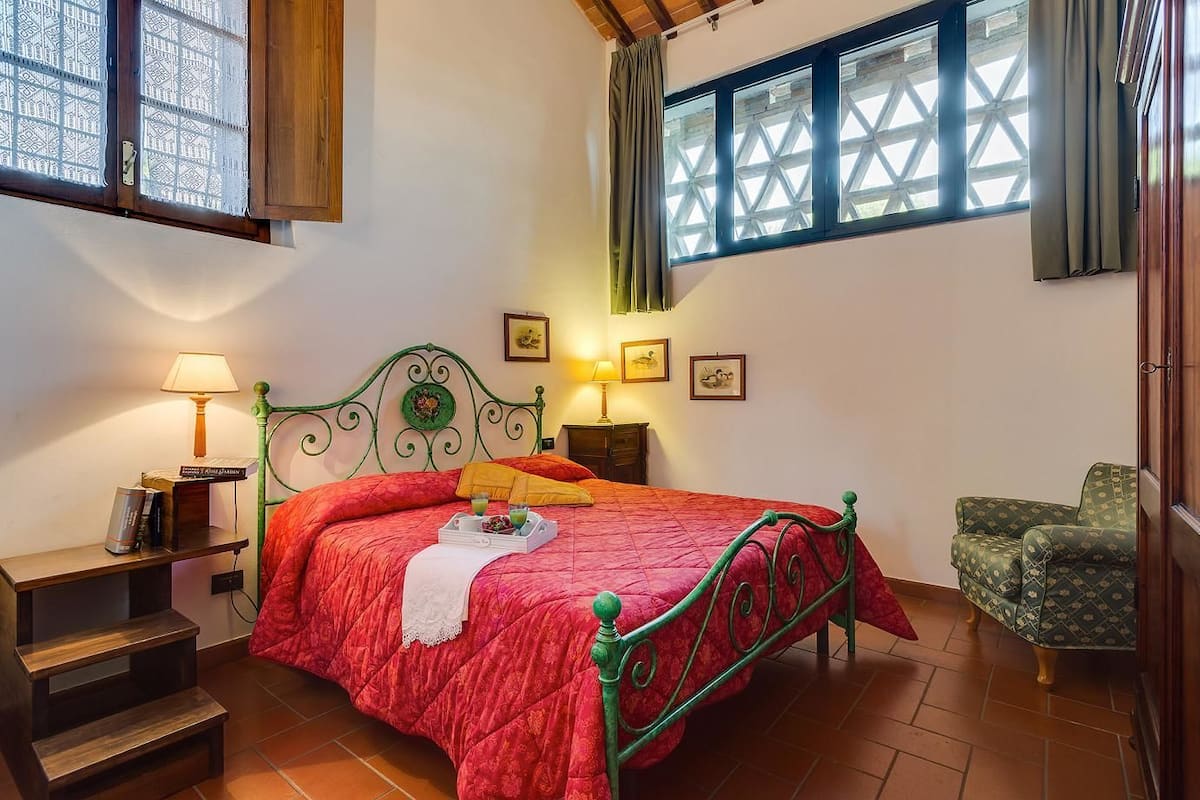 Un dormitorio con cama, mesitas de noche, una silla y ventana con vistas.