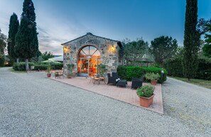 A stone building with a large arched entrance, outdoor seating with chairs and tables, and potted plants. - Relais Antico Borgo San Lorenzo (Poggibonsi)