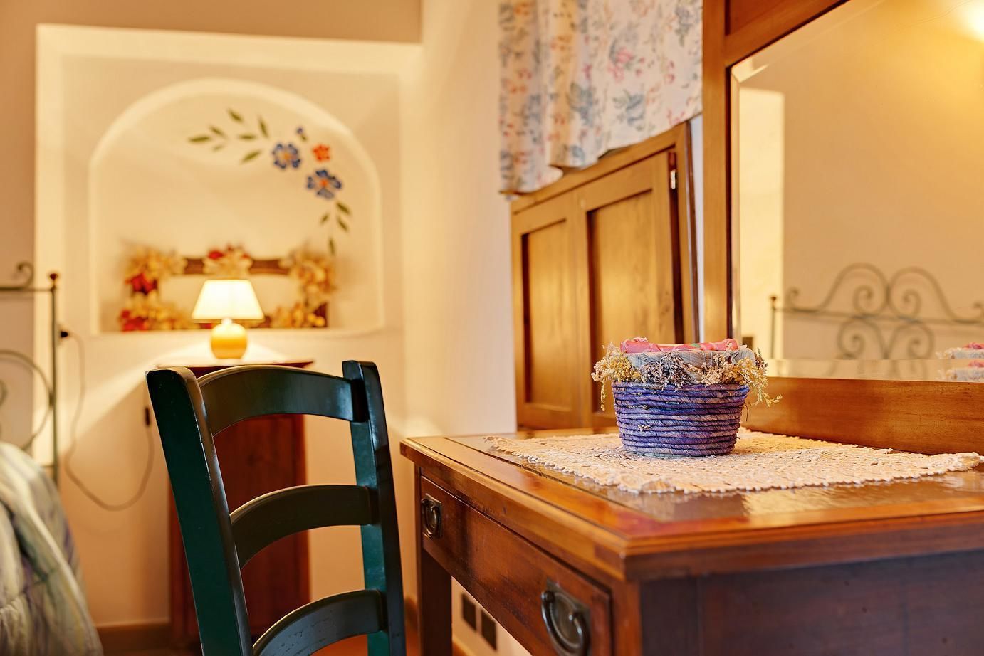 A wooden dresser with a woven basket on top, a chair, a lamp, and a floral wall decoration.