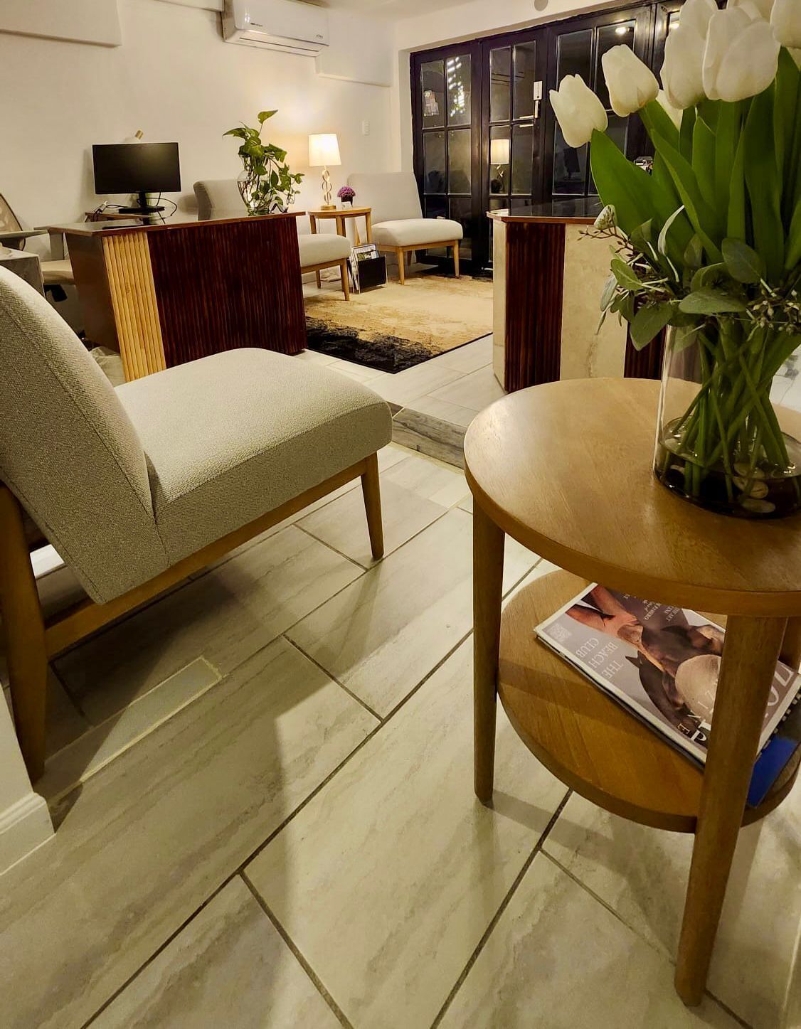 A living room with a sofa, a coffee table, a TV, and a window with white tulips.