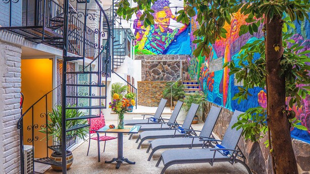 A courtyard with a mural, outdoor seating, and a staircase. - ZonaZ Boutique Hotel (Puerto Vallarta)