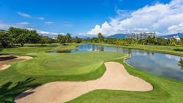 A golf course with a pond, sand bunkers, and palm trees.