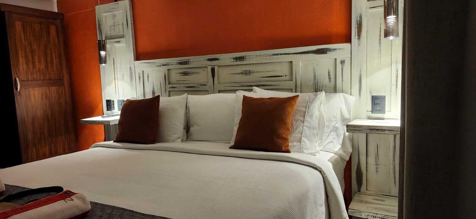 Una habitación de hotel con una cama, ropa de cama blanca y un cabecero de madera.