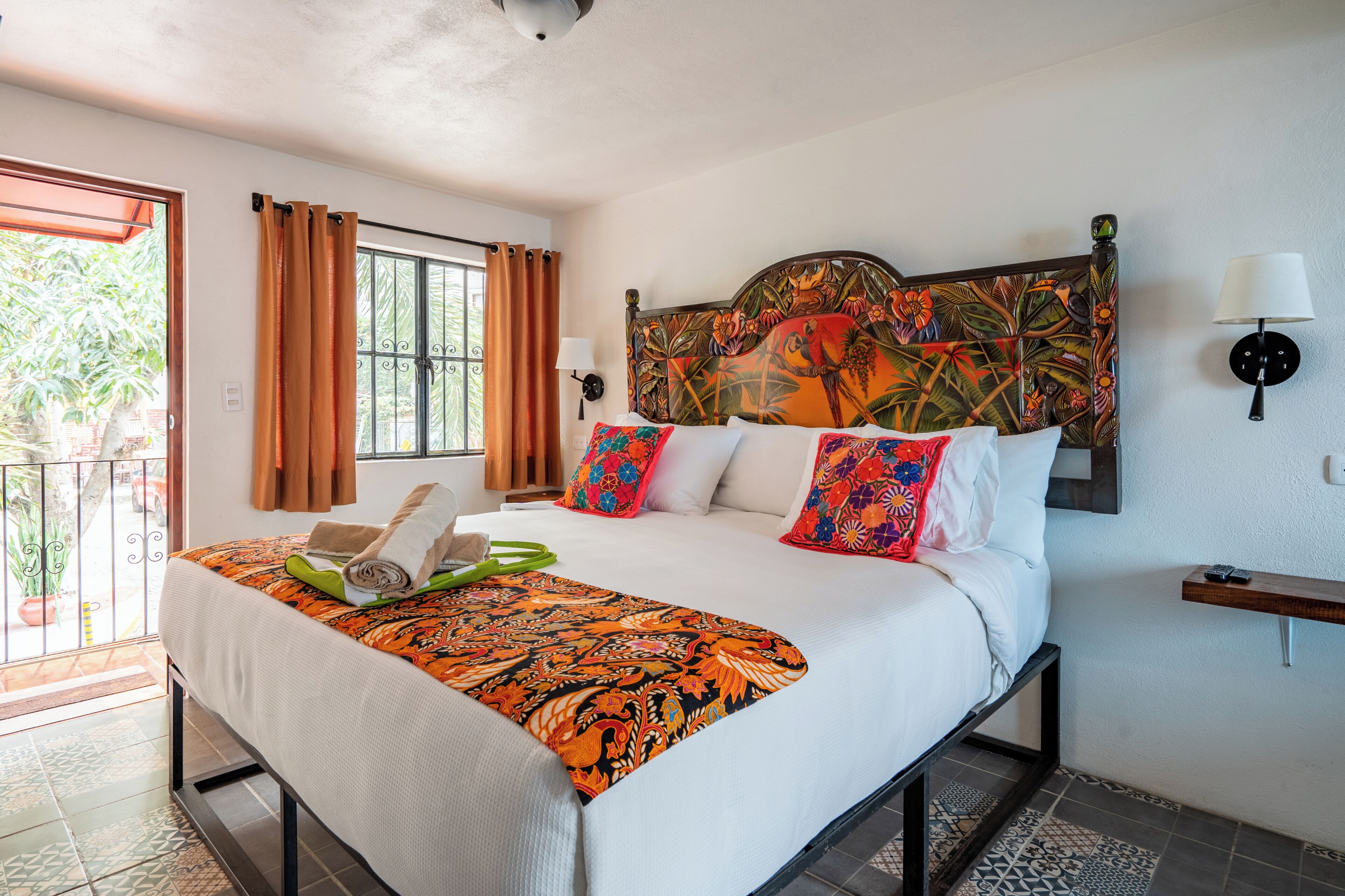 Habitación de hotel con cama, cortinas, cabecero con diseño floral, mesita de noche y vistas por la ventana.