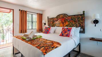 Ein Hotelzimmer mit Bett, Vorhängen, einem Blumenmuster-Kopfstütze, einem Nachttisch und Blick durch ein Fenster.