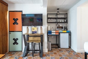 A compact kitchen with a bar stool, a refrigerator, a microwave, and a small fridge.