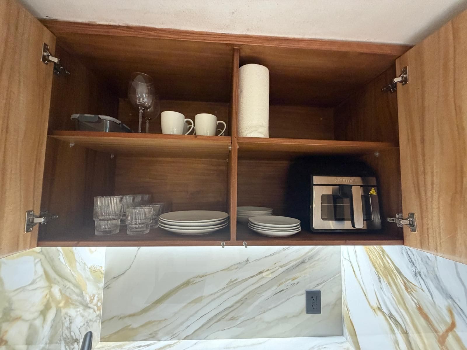 A wooden cabinet with shelves containing kitchenware, a microwave, and a marble countertop.