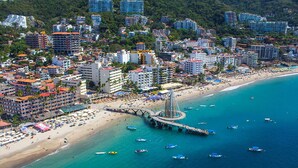 An aerial view of a coastal city with a beach, numerous buildings, and a prominent pier structure. - ZonaZ Boutique Hotel (Puerto Vallarta)