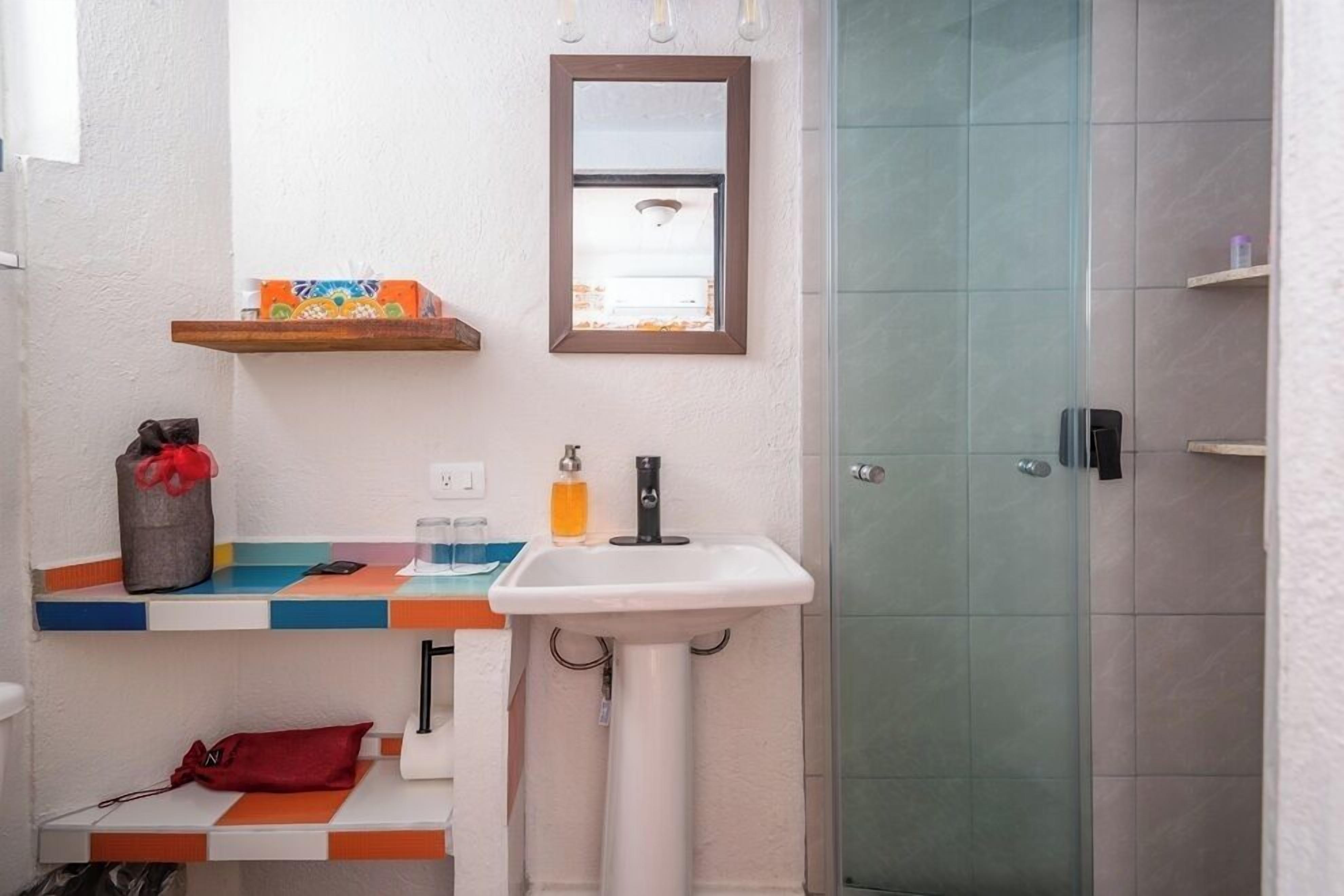 Une salle de bain avec un lavabo blanc, un miroir, une douche et une étagère contenant des articles de toilette.