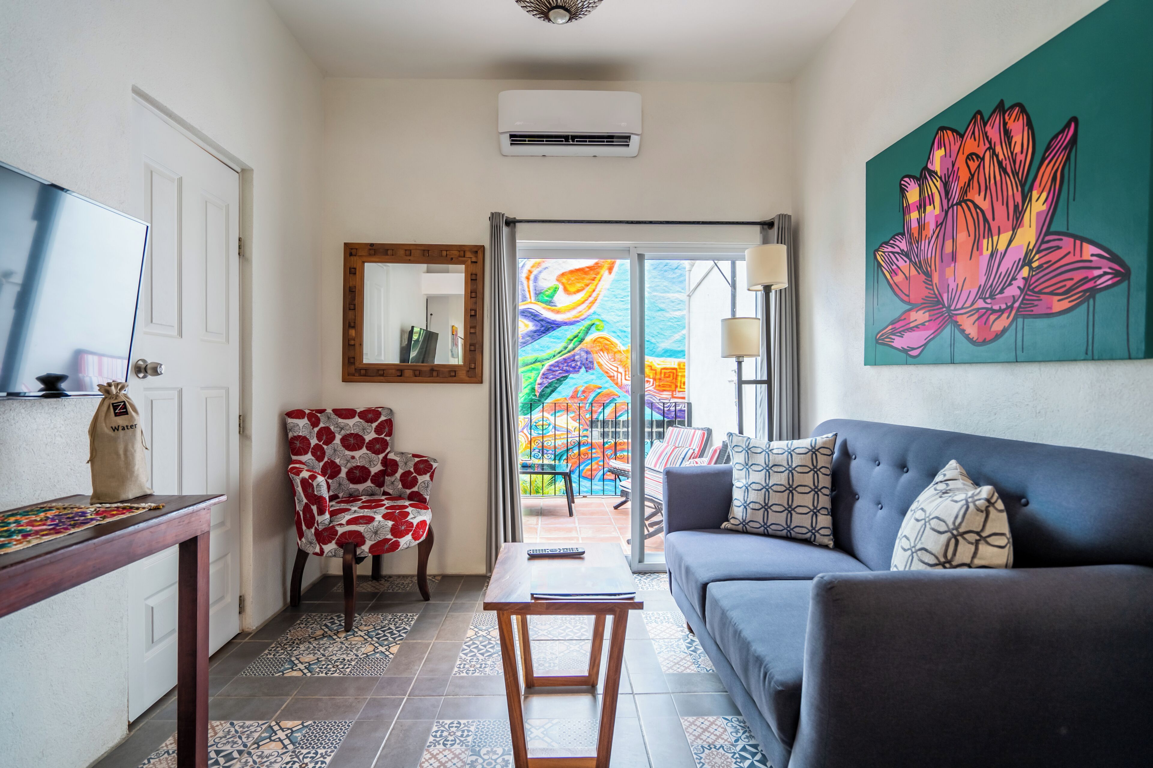 A living room with a sofa, a chair, a table, a TV, and a colorful artwork on the wall.
