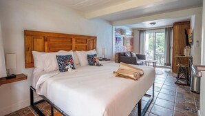 A hotel room with a large bed, a wooden headboard, a small desk with a lamp, a chair, and a view of the outdoors. - ZonaZ Boutique Hotel (Puerto Vallarta)