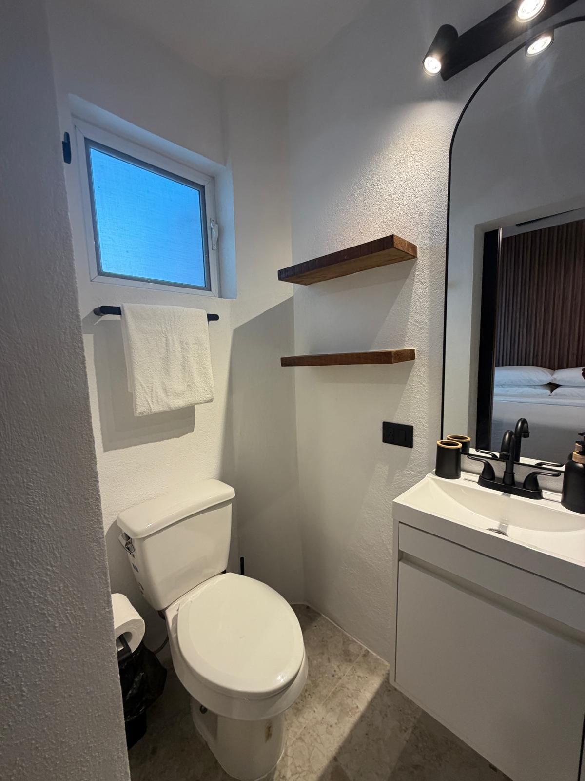 A compact bathroom with a toilet, a sink, a mirror, and a window.