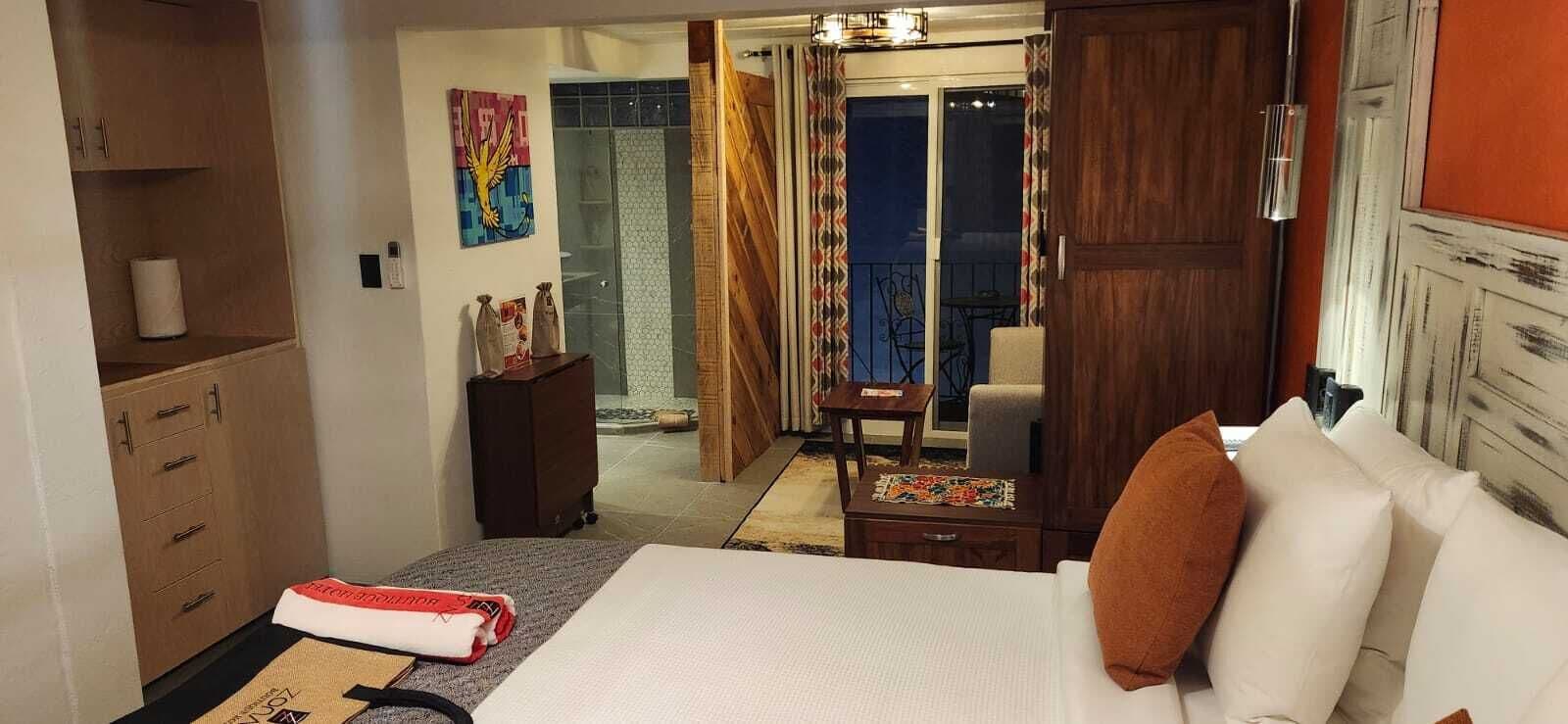 A hotel room with a bed, a wooden wardrobe, a small table, and a mirror.