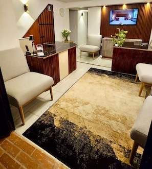 A modern living room with a sofa, a coffee table, a TV mounted on the wall, and a reception desk.