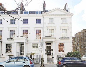 A row of white townhouses with a central building featuring a pedimented entrance and a balcony.