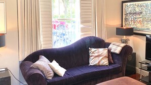 Ein Wohnzimmer mit einem violetten Sofa, einem Hocker, einem Fernseher und einem Gemälde an der Wand.