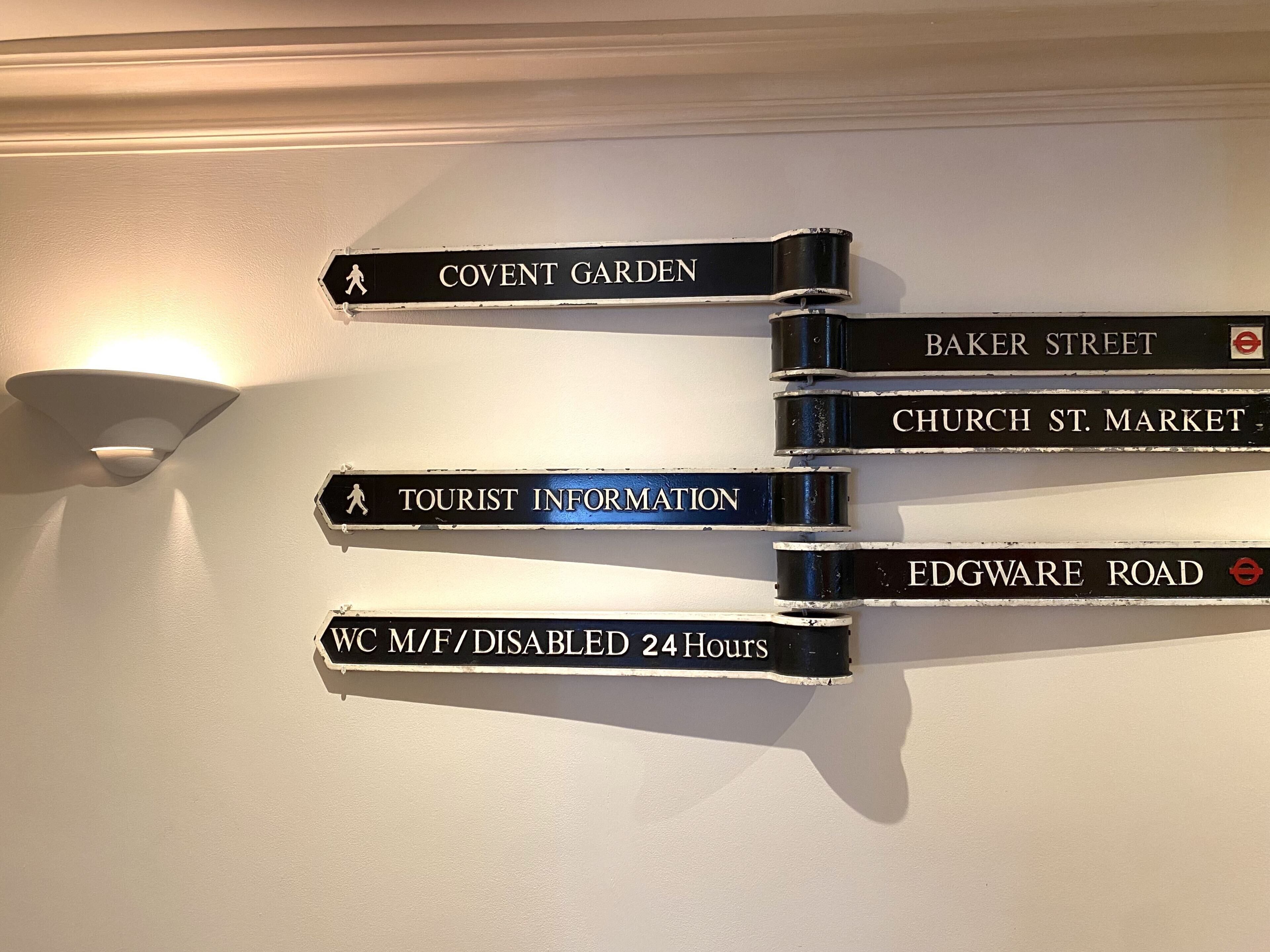 En vejskilte med flere destinationer, herunder 'COVENT GARDEN', 'BAKER STREET', 'CHURCH ST. MARKET', 'TOURIST INFORMATION' og 'FDGWARE ROAD'.