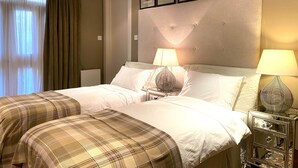 Ein Hotelzimmer mit Doppelbett, zwei Nachttischen mit Lampen, einem großen Fenster mit Vorhängen und gerahmten Bildern an der Wand.