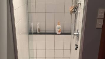 Un espace douche avec des carreaux blancs, une porte en verre et une étagère contenant des articles de toilette.