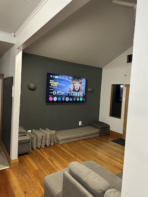 A modern living room with a flat-screen TV mounted on a dark wall, a grey sofa, and a wooden floor. - Character bungalow in the heart of Blenheim (Blenheim)