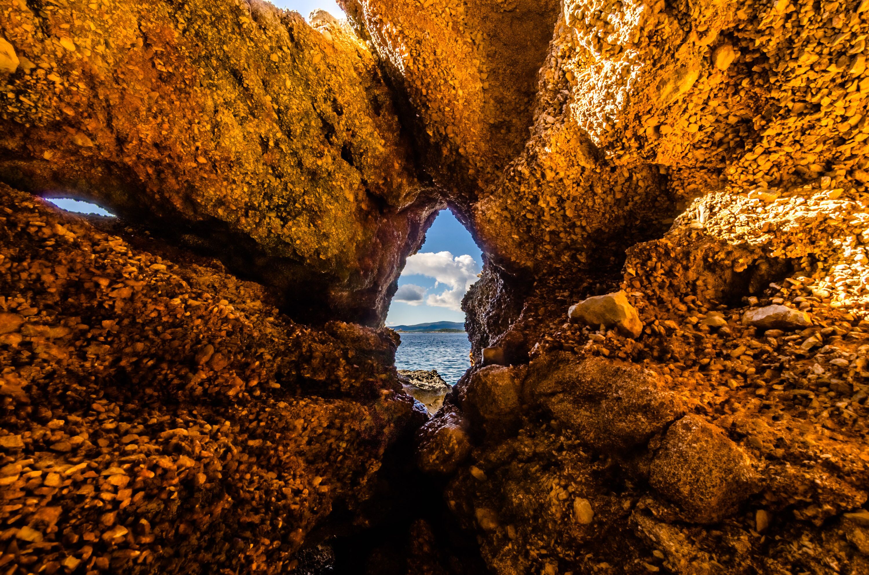 A natural rock formation with a narrow opening leading to a body of water.