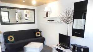 Ein modernes Wohnzimmer mit einer schwarzen Couch, einem weißen Couchtisch, einem Flachbildfernseher, einer Stereoanlage und einem Spiegel.