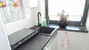 Eine Küche mit schwarzem Arbeitsplatz, einem Spülbecken, einem Wasserhahn, einer grünen Flasche und einem Blumentopf.
