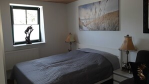 Ein Schlafzimmer mit einem Bett, zwei Nachttischlampen, einem Fenster mit Blick und einem Bild an der Wand.