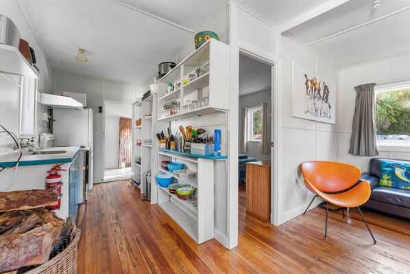 A modern kitchen with white cabinetry, wooden flooring, and a dining area with a blue sofa and orange chair.