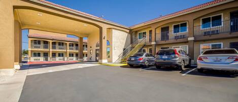 A multi-story hotel with a covered parking area, multiple balconies, and a clear blue sky.