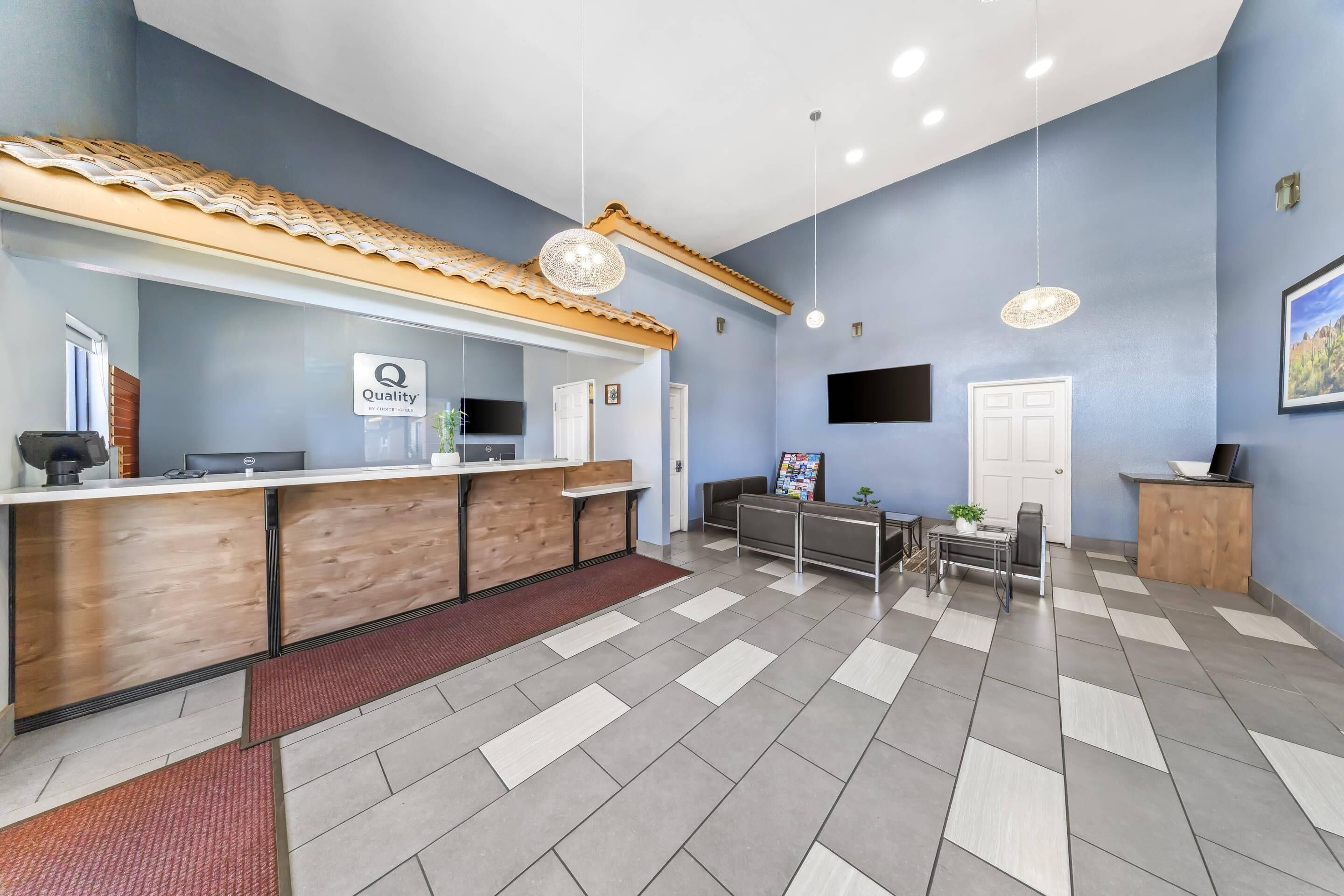 A reception area with a wooden reception desk, a sign reading 'Quality,' a flat-screen TV, and a tiled floor.