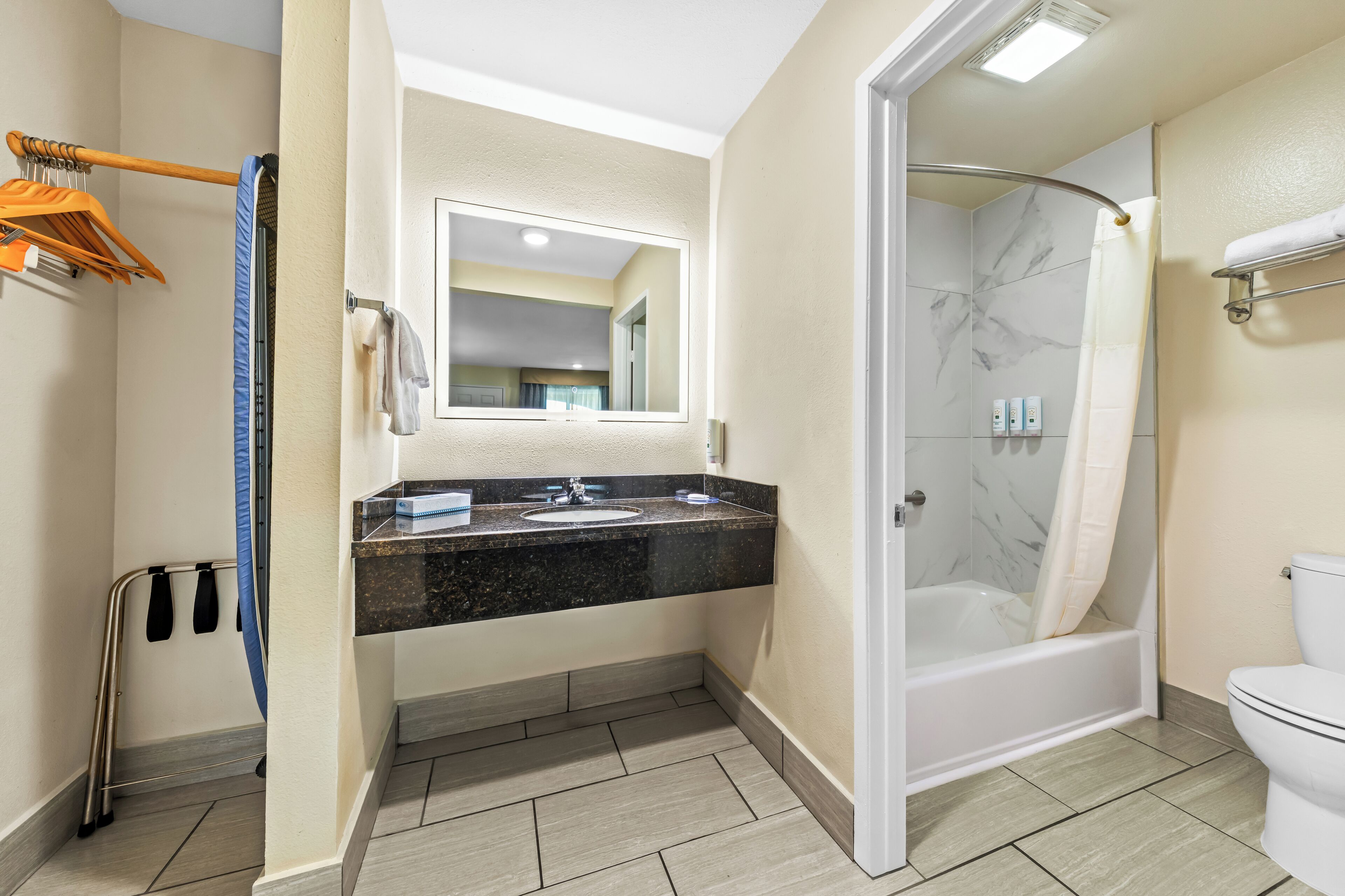 A bathroom with a marble shower, a sink with a black countertop, and a toilet.