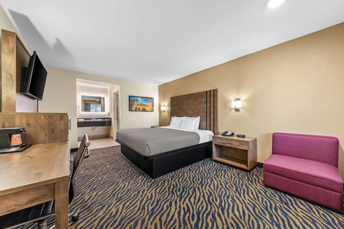 A hotel room with a bed, a desk, a TV, a chair, and a painting on the wall.