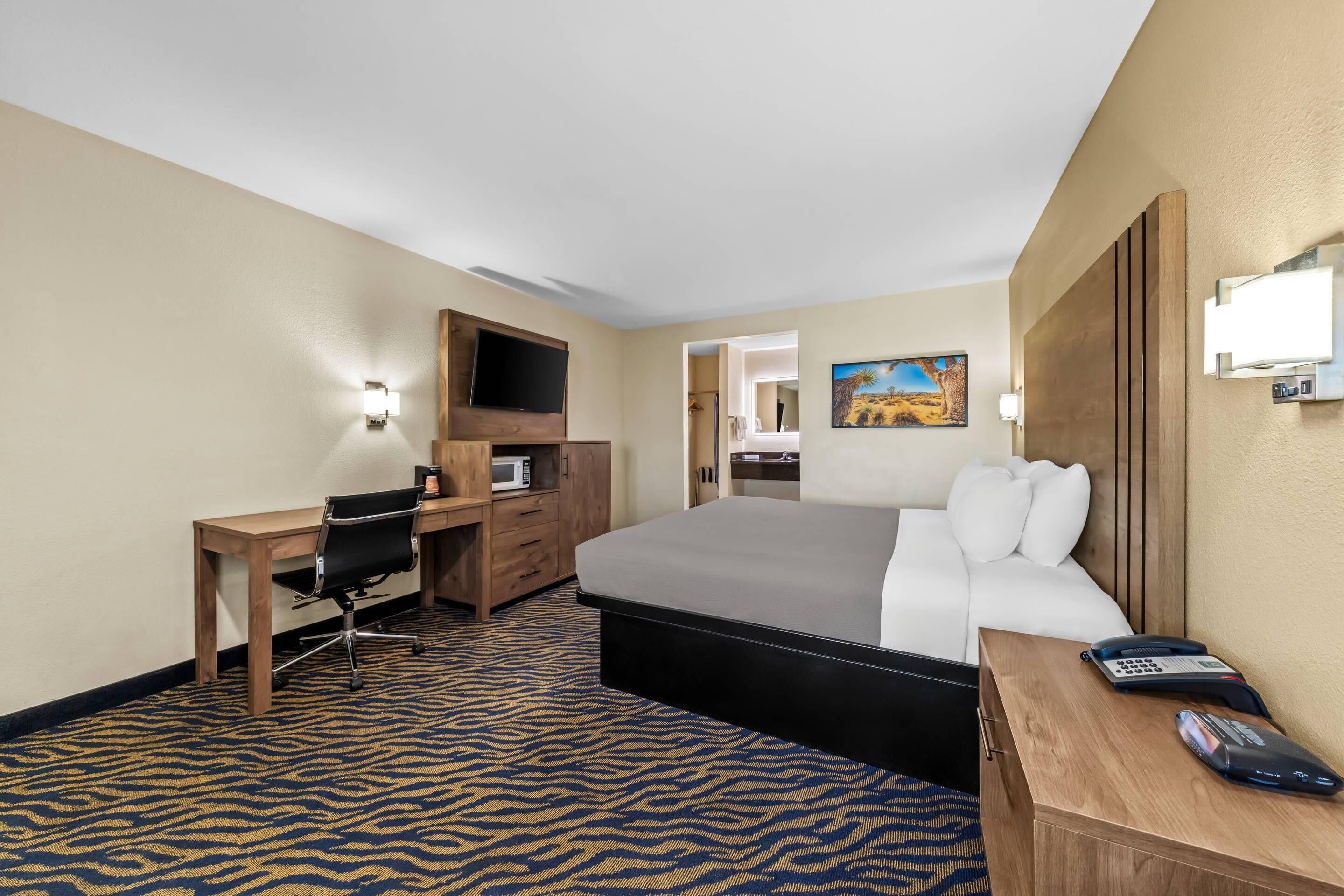 A hotel room with a bed, desk, chair, and a television.