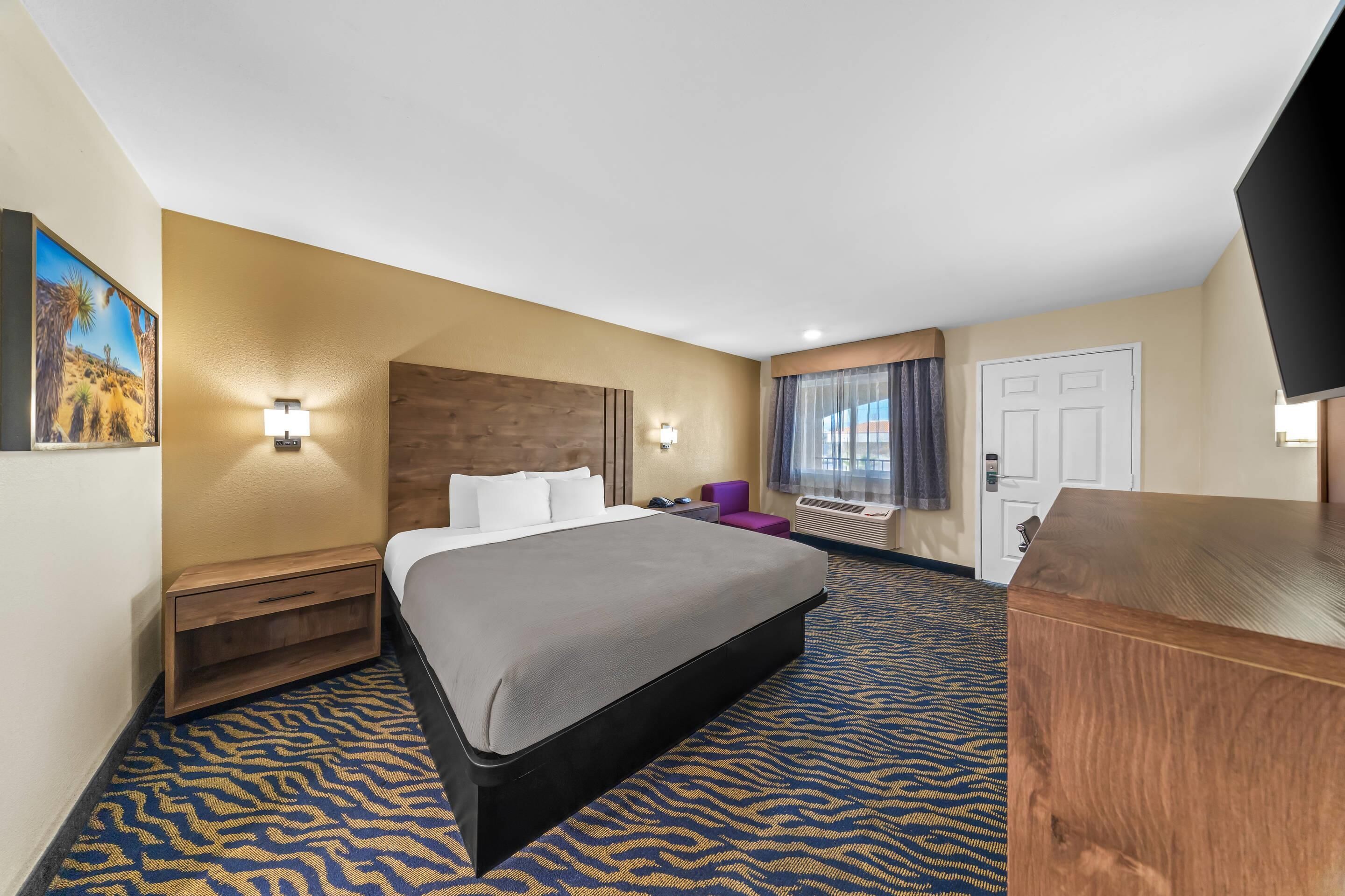 A hotel room with a bed, nightstand, desk, and a television.
