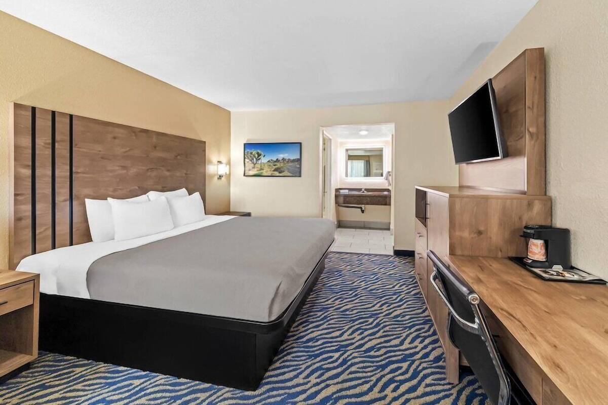 A hotel room with a bed, desk, chair, TV, and a painting on the wall.